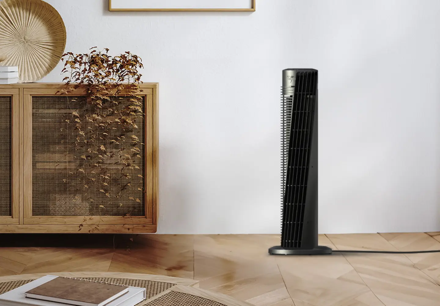 OSC54 Tower Fan Lifestyle Lifestyle image of OSC54 tower fan. The fan is in a room with a grey wall, wood floor and a wicker cabinet and coffee table. The tower fan's cord goes off to the right, indicating it is plugged in